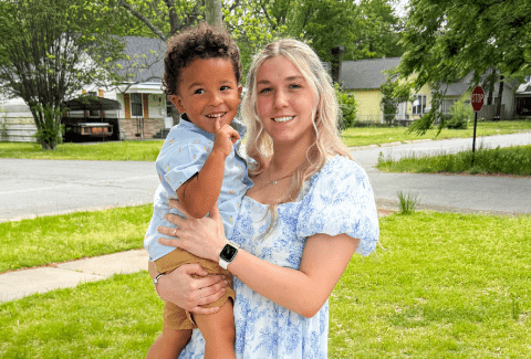 Karmen holds her boy toddler on her hip outside