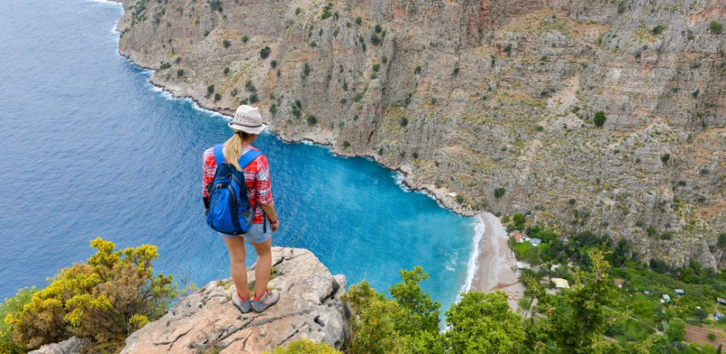 Hiking woman standing at cliff viewing a beautiful blue sea and mountain.