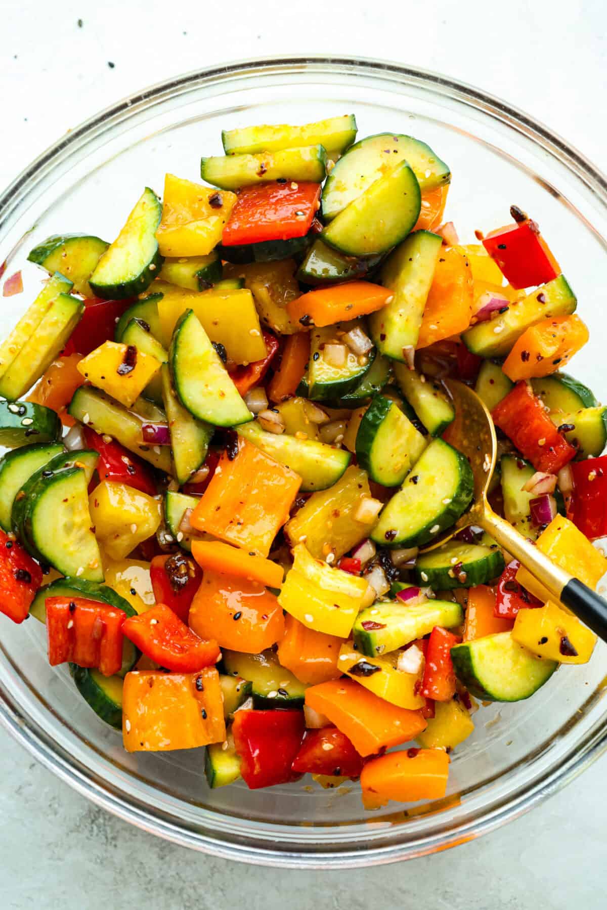 I don’t know what kind of hold cucumbers have on me lately, but I’m obsessed. This cucumber bell pepper salad is crunchy, a little sweet, a little spicy, and totally guilt-free. Veggies and dressing mixed together in a bowl to make the cucumber and bell pepper salad.