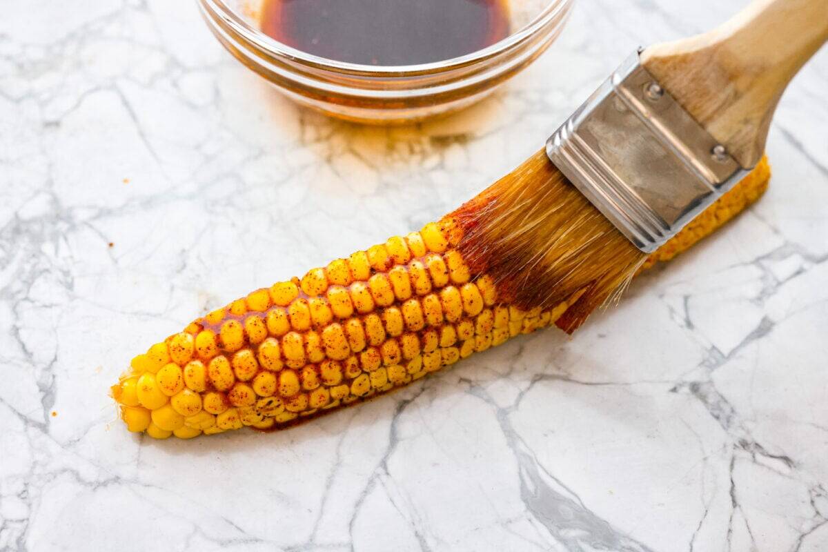 I had to try these viral Corn Ribs, and now I totally get the hype! They're fun, handheld, and smothered in creamy, zesty Mexican street corn flavor. Make a batch to share... or don’t. I won’t judge. Someone brushing the corn rib with marinade.