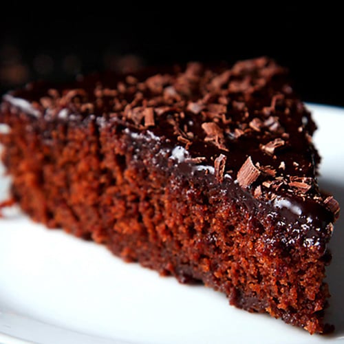 A triangular slice of eggless chocolate cake on a white plate.
