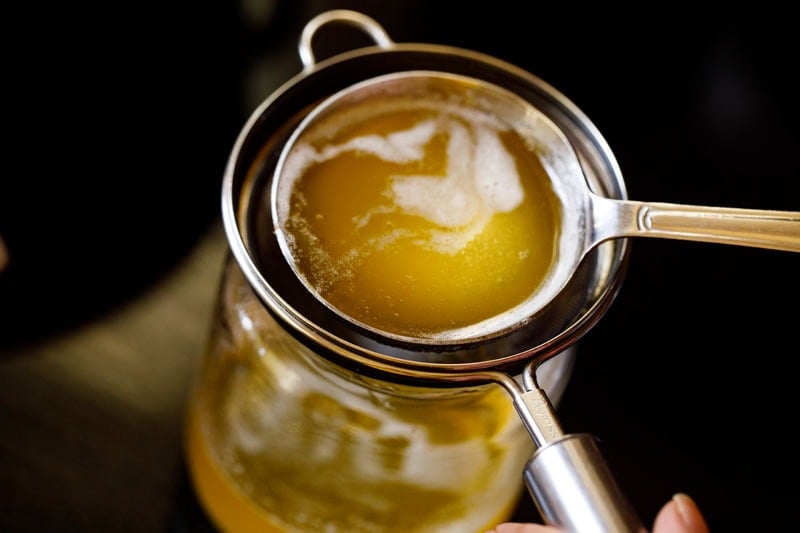 ladle pouring ghee through a strainer into a glass jar showing how to make ghee.