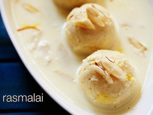 rasmalai in an oblong white serving dish covered with thickened milk and garnished with sliced almonds and saffron threads.