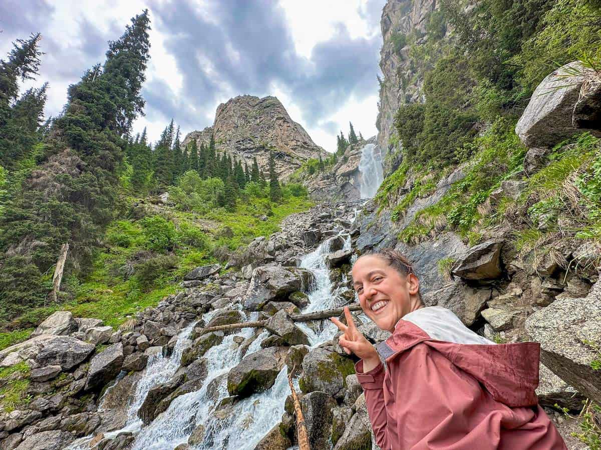 female hiker posing at the top of Barskoon Waterfall in Kyrgyzstan