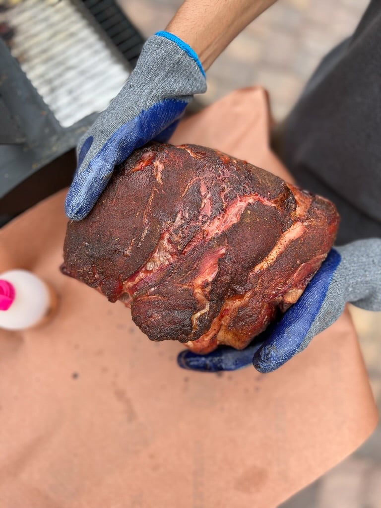 Hands holding smoked pork butt.