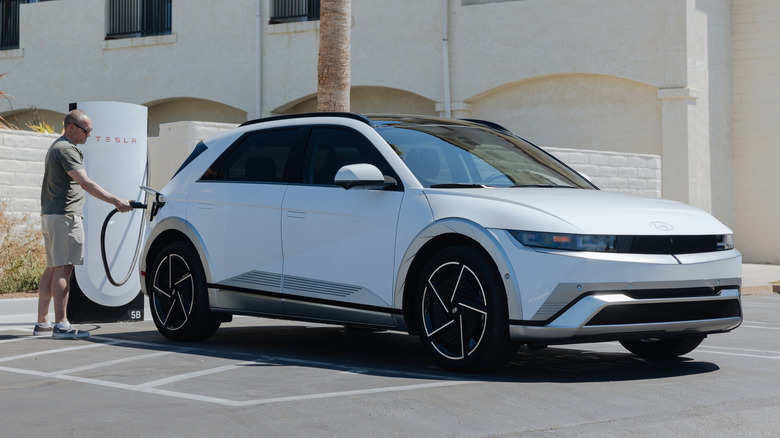 a man plugging a white Ioniq 5 into a Tesla charger